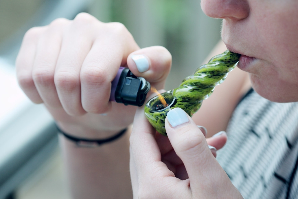 Gender neutral smoker who has been cultivating homegrown hemp lights cannabis in a glass pipe outdoors. Cultivating Homegrown Hemp vs. Marijuana While Keeping THC in Check